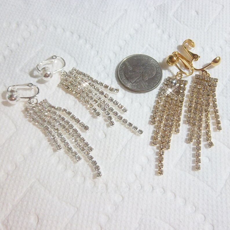 May include: A pair of silver and gold clip-on earrings with dangling crystal strands. The earrings are shown next to a US quarter for size reference.