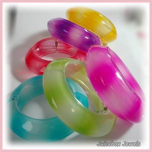 May include: A collection of colorful, translucent bangles in shades of yellow, purple, pink, red, green, and turquoise. The bangles are made of a smooth, glossy material and are stacked together. The text "Juicebox Jewels" is visible in the bottom right corner.