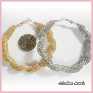 May include: A pair of hoop earrings, one gold-toned and one silver-toned, with a woven, twisted design. A US quarter is placed between the earrings for size comparison. The earrings are from Juicebox Jewels.