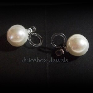 May include: A pair of clip-on earrings with large, white pearl-like beads. The earrings have clear plastic clips.