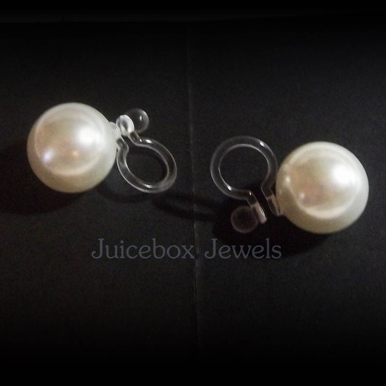 May include: A pair of clip-on earrings with large, white pearl-like beads. The earrings have clear plastic clips.