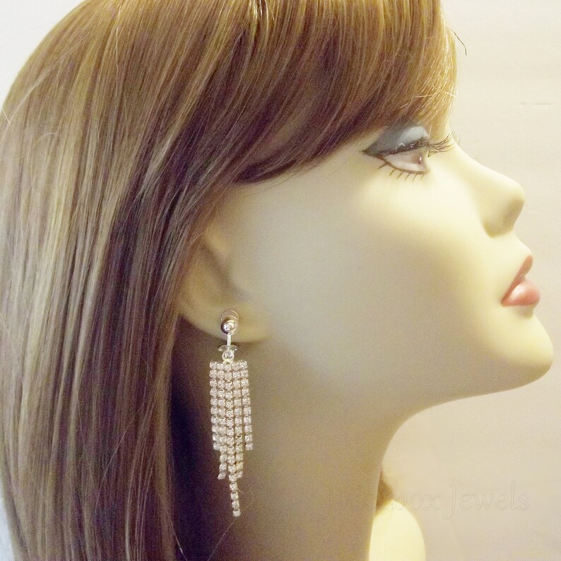 May include: A pair of silver dangle earrings with a cascade of clear rhinestones. The earrings are clip-on style.