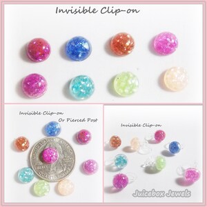 May include: A collection of colorful, round clip-on earrings in various colors, including pink, blue, orange, and green. The earrings are shown with a quarter for size comparison. The text "Invisible Clip-on" and "Juicebox Jewels" are also visible.