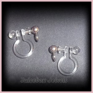 May include: A pair of clear plastic earring clips with silver metal balls and posts. The clips are designed to hold earrings in place without piercing the ear.