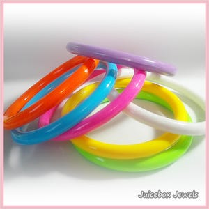 May include: A collection of colorful bangles in various shades, including orange, blue, pink, yellow, green, white, and purple. The bangles are stacked and intertwined, creating a vibrant display. The image is well-lit, highlighting the glossy finish of the bracelets.