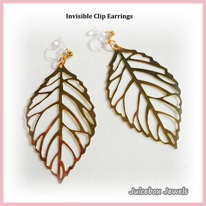 May include: A pair of gold-colored leaf-shaped clip earrings. The earrings are made of a thin metal with intricate cut-out details. The text "Invisible Clip Earrings" is at the top, and "Juicebox Jewels" is at the bottom.