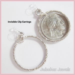 May include: Two silver-toned invisible clip earrings. One earring features a quarter coin set within a textured silver frame. The other earring is a textured silver hoop. The text "Invisible Clip Earrings" is visible.