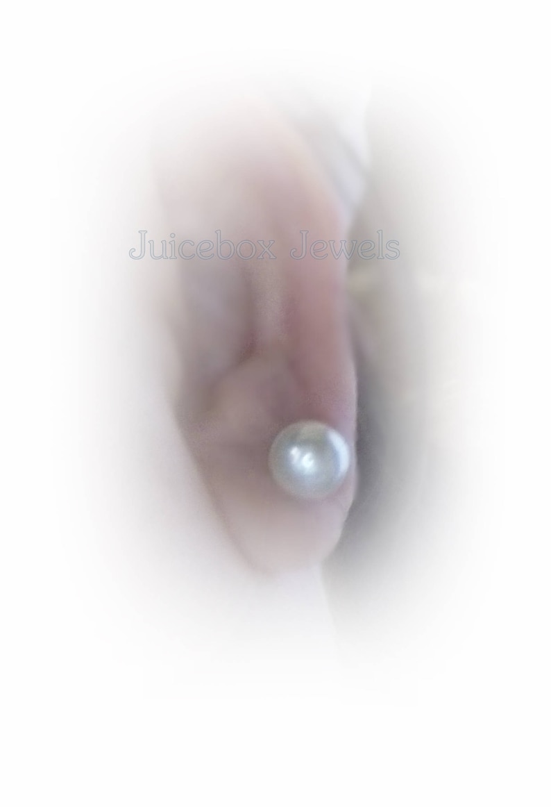 May include: A close-up of a person's ear with a single pearl earring. The pearl is white and round.