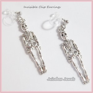 May include: A pair of silver skeleton clip-on earrings. The earrings are attached to clear plastic clips. The earrings are labeled "Invisible Clip Earrings" and "Juicebox Jewels".