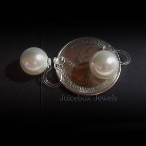 May include: A pair of white pearl clip-on earrings, shown next to a US quarter for size comparison. The earrings are made with clear plastic clips.