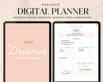 Op de afbeelding: Een digitale planner voor 2023 met een roze achtergrond en het woord "Dreamer" in witte tekst. De planner bevat een dagelijkse plannerpagina met secties voor de datum van vandaag, bevestiging, top 3 prioriteiten, gebeurtenissen, taken, stemming en reflectie. De tekst "Ik ben dankbaar voor mijn gezondheid" staat in de sectie reflectie.