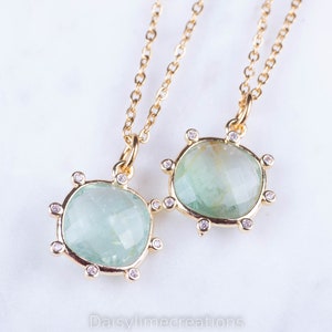 May include: Two gold necklaces with green gemstone pendants. Each pendant is surrounded by small clear stones.