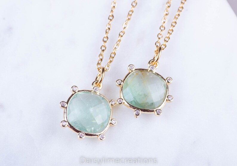 May include: Two gold necklaces with green gemstone pendants. Each pendant is surrounded by small clear stones.
