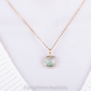 May include: A gold chain necklace with a light green gemstone pendant surrounded by small clear stones.