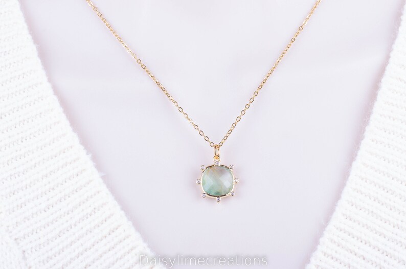 May include: A gold chain necklace with a light green gemstone pendant surrounded by small clear stones.