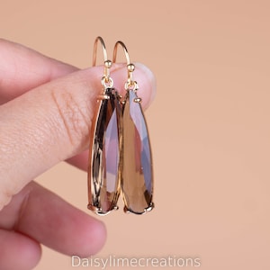 May include: A pair of gold dangle earrings with teardrop-shaped brown gemstone accents.