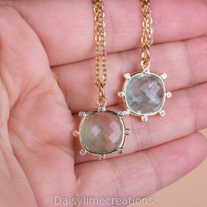 May include: Two gold necklaces with green gemstone pendants surrounded by small clear stones. The pendants are different sizes.