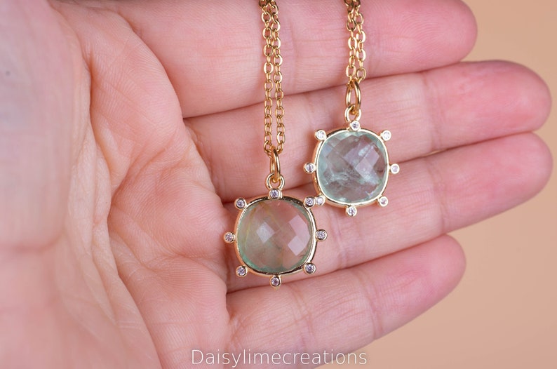 May include: Two gold necklaces with green gemstone pendants surrounded by small clear stones. The pendants are different sizes.
