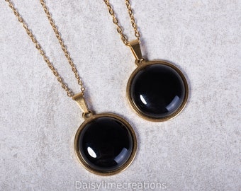 May include: Two gold necklaces with black round pendants. The pendants have a gold rim around the black glass.