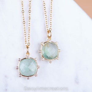 May include: Two gold necklaces with green gemstone pendants. Each pendant is surrounded by small clear stones.