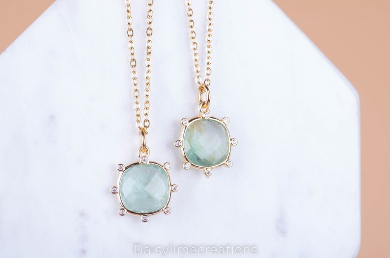 May include: Two gold necklaces with green gemstone pendants. Each pendant is surrounded by small clear stones.