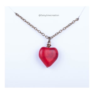 Peut inclure: Un collier avec un pendentif en forme de cœur rouge sur une chaîne en bronze. Le pendentif est fait d'une pierre rouge lisse.