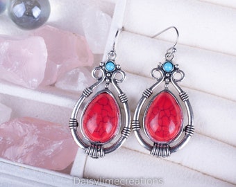 Puede incluir: Un par de pendientes de plata con piedras rojas y turquesas. Los pendientes tienen forma de lágrima y están engastados en un marco de plata.