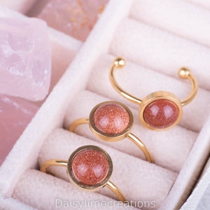 Peut inclure: Trois bagues en or avec des pierres précieuses rondes rouges dans un écrin à bagues en velours blanc. Les bagues sont disposées en rangée, la plus grande à l'arrière et la plus petite à l'avant.