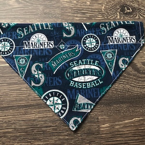 May include: A blue and green dog bandana with the Seattle Mariners logo and the words "Seattle Mariners Baseball".