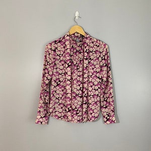 May include: A long-sleeved blouse with a high neck and a pink and white floral print. The blouse has a tie at the neck.