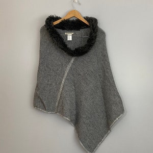 May include: Gray knitted poncho with a black faux fur collar. The poncho has a diagonal seam and a fringed edge.