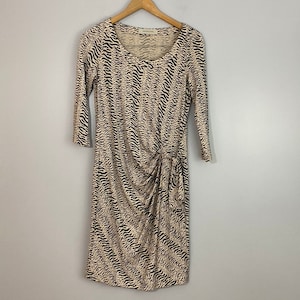 Può includere: Un abito beige e nero con stampa animalier, scollo rotondo e maniche a 3/4. L'abito ha un dettaglio drappeggiato in vita.