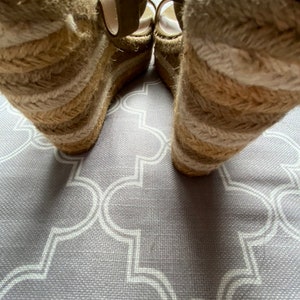 May include: A pair of beige wedge sandals with a woven jute platform. The sandals have a strap that goes around the ankle and a buckle closure.