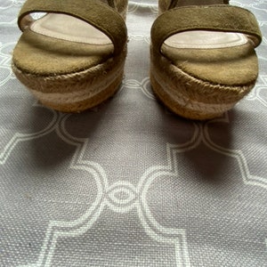 May include: A pair of olive green suede wedge sandals with a woven jute platform and ankle straps.