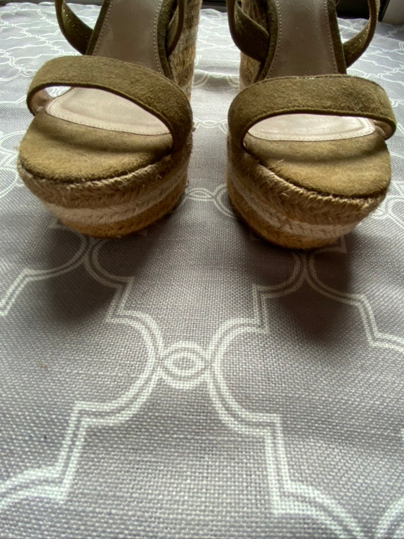 May include: A pair of olive green suede wedge sandals with a woven jute platform and ankle straps.