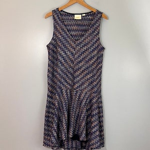 May include: A sleeveless, V-neck dress with a chevron pattern in shades of blue, brown, and white. The dress has a high-low hemline and is made of a soft, stretchy fabric.