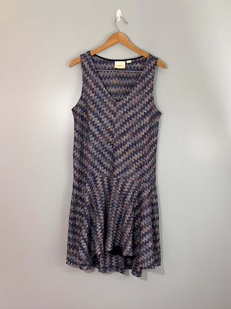 May include: A sleeveless, V-neck dress with a chevron pattern in shades of blue, brown, and white. The dress has a high-low hemline and is made of a soft, stretchy fabric.