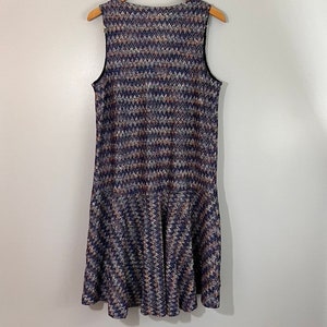 May include: A sleeveless dress with a chevron pattern in shades of blue, brown, and white. The dress has a ruffled hem.