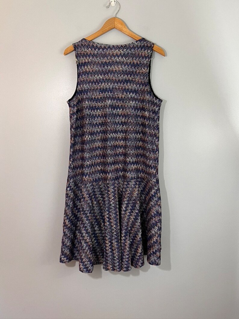 May include: A sleeveless dress with a chevron pattern in shades of blue, brown, and white. The dress has a ruffled hem.