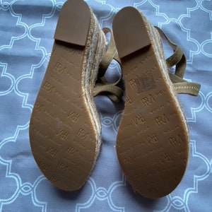 May include: A pair of brown espadrille wedge sandals with a woven jute platform and leather straps. The sandals have the text "PA PELLE MODA" printed on the soles.