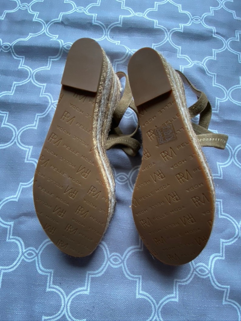May include: A pair of brown espadrille wedge sandals with a woven jute platform and leather straps. The sandals have the text "PA PELLE MODA" printed on the soles.