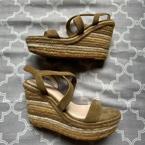 May include: A pair of brown suede wedge sandals with a woven jute platform. The sandals have a strap across the foot and an ankle strap.