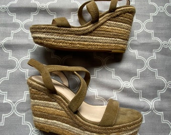 Könnte beinhalten: Ein Paar braune Wildledersandalen mit Keilabsatz und einer geflochtenen Juteplattform. Die Sandalen haben einen Riemen über dem Fuß und einen Knöchelriemen.