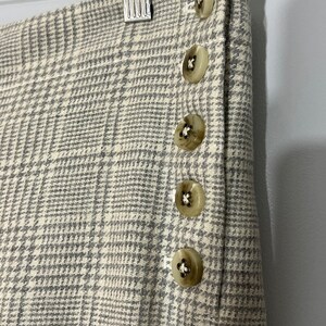 Peut inclure: Gros plan sur une jupe en tissu &agrave; carreaux blanc et gris avec une rang&eacute;e de cinq boutons beiges sur le c&ocirc;t&eacute;.