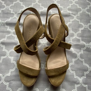 May include: A pair of olive green suede wedge sandals with criss-cross straps and the brand name "Pelle Moda" on the insole.