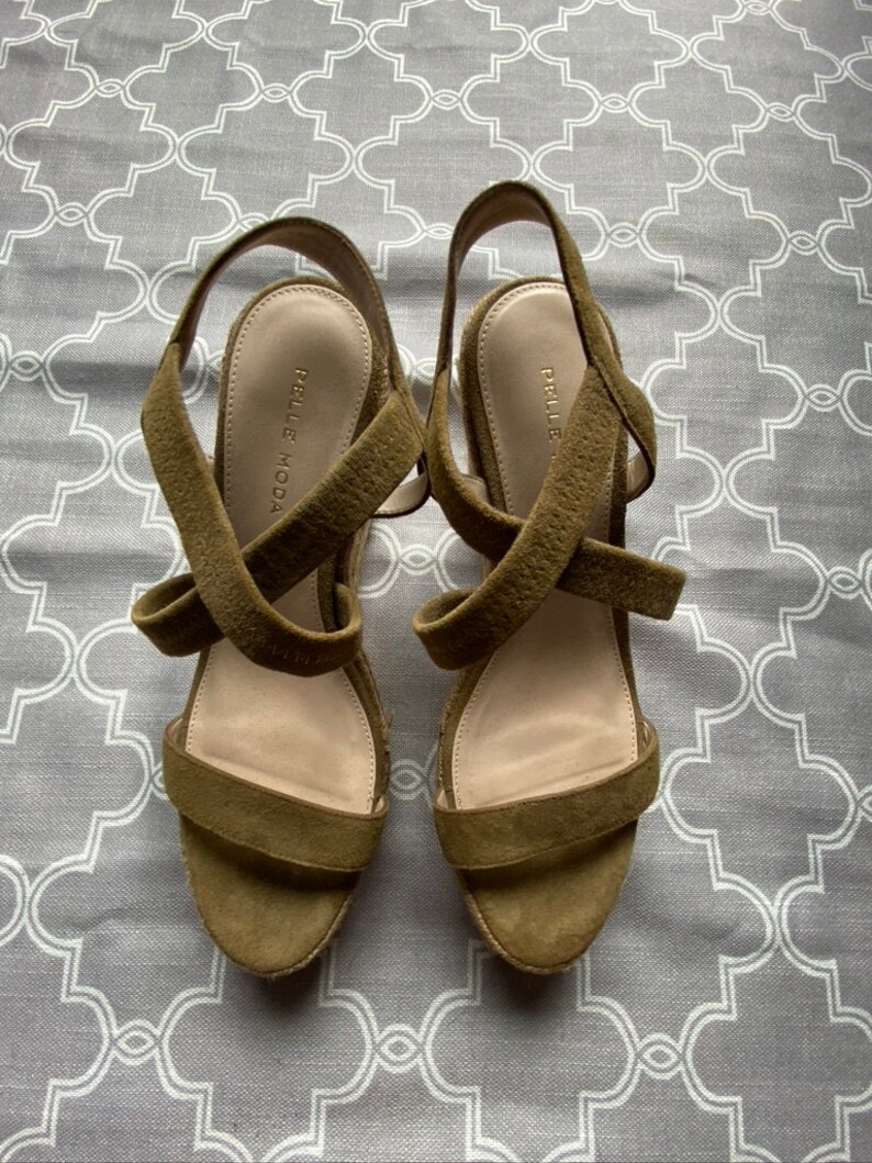 May include: A pair of olive green suede wedge sandals with criss-cross straps and the brand name "Pelle Moda" on the insole.