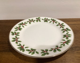 May include: A white ceramic plate with a gold rim and a green holly leaf and red berry design around the edge.