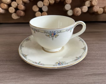 May include: A white teacup and saucer with a gold rim and floral pattern. The cup has a handle and the saucer has a scalloped edge.