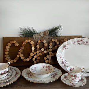 Könnte beinhalten: Ein Set aus weißem Porzellan-Geschirr mit Blumenmuster. Das Set beinhaltet eine große ovale Servierplatte, zwei Speiseteller, zwei Suppenschalen, zwei Teetassen und zwei Untertassen. Das Geschirr ist mit einem zarten rosa und weißen Blumenmuster verziert.