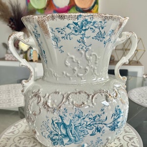 May include: A white ceramic vase with blue and gold floral designs. The vase has two handles and a wide mouth.